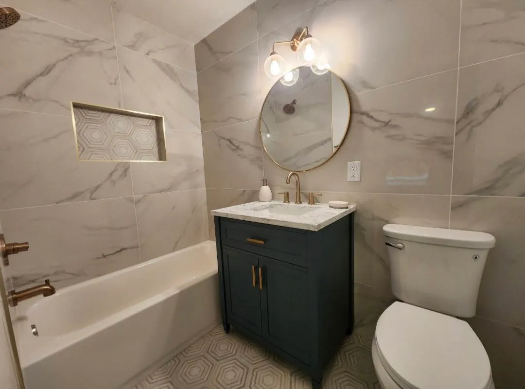 Marble-look tile bathroom with navy vanity and gold fixtures