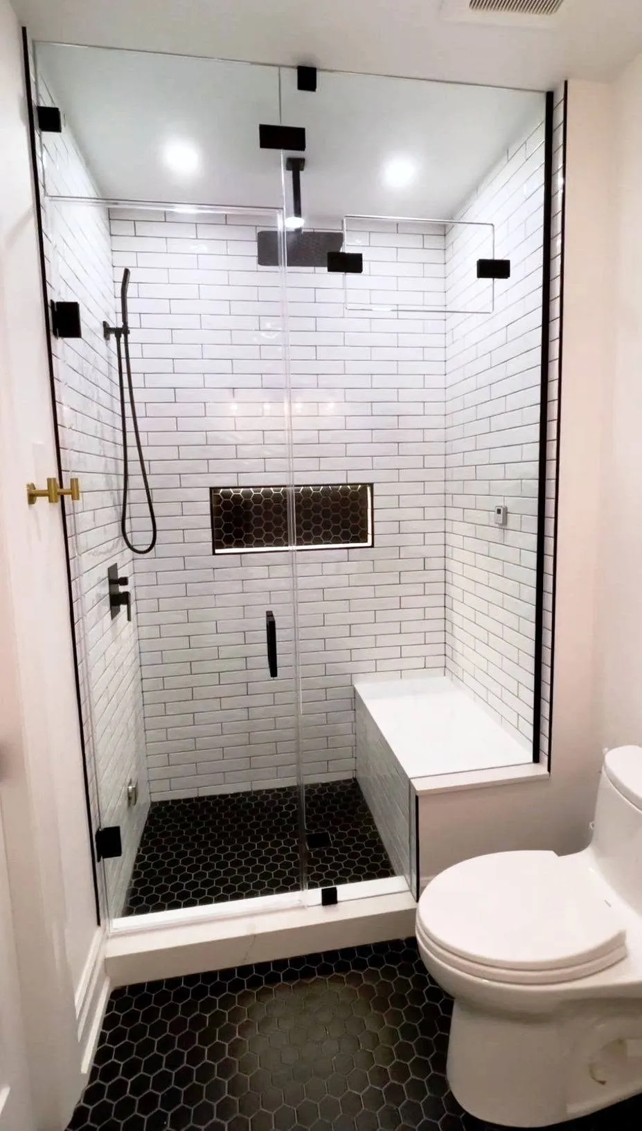 Walk-in shower with white subway tile, black hex floor, lighted niche and frameless glass