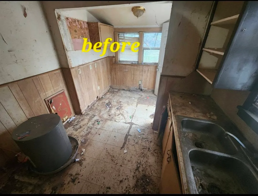 Kitchen before rehab with damaged floors, old cabinets and debris