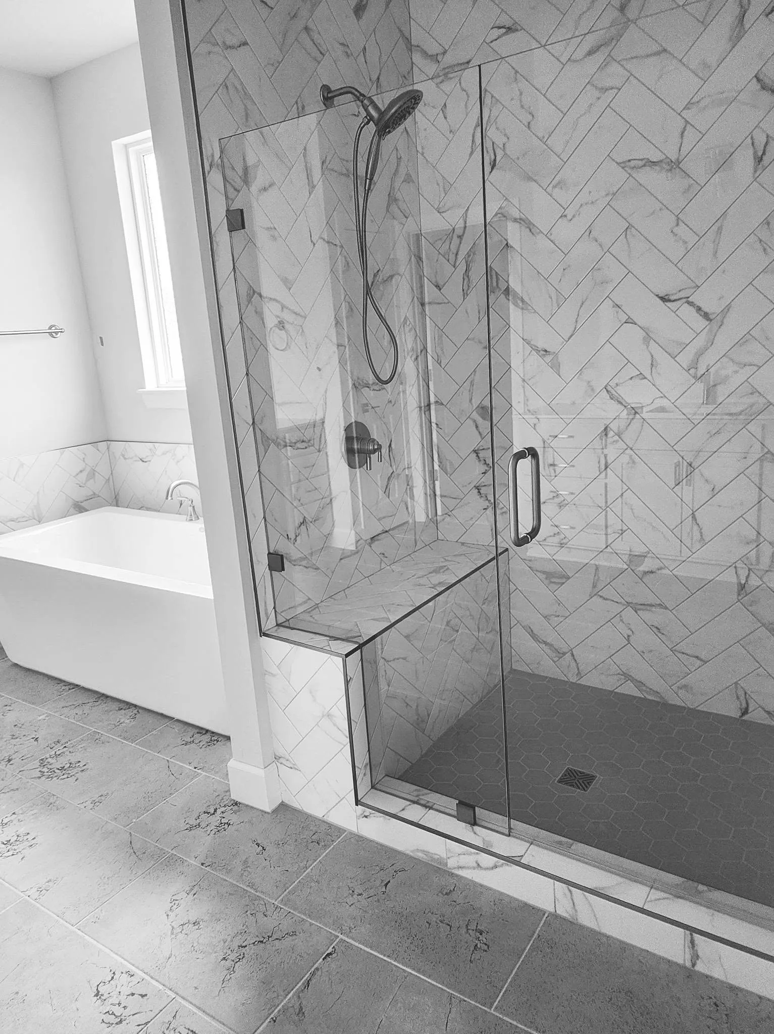 Herringbone marble-look shower tile with a built-in bench and hex tile floor
